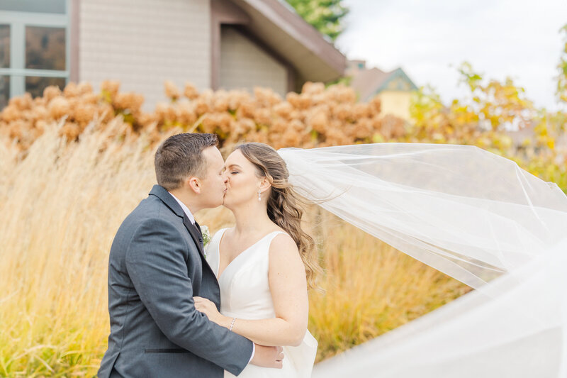 Newlyweds kiss in a windy garden as the veil flies around them