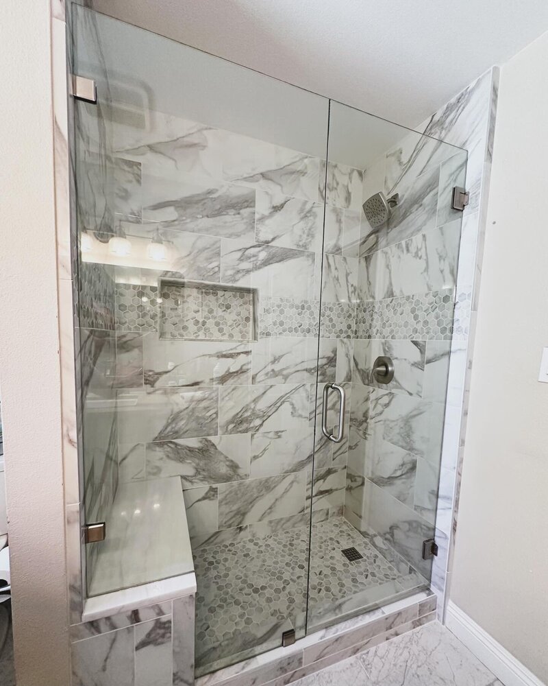 A modern white and grey marble shower tile, with a seat and new clear glass shower enclosure.