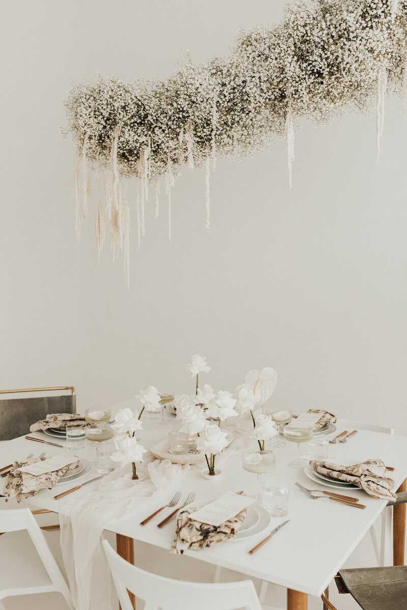 table and chairs set with a modern neutral tablescape with single stem roses and a baby's breath hanging arch above