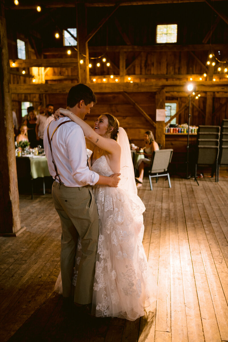 Newlyweds share their first dance in a rustic barn venue illuminated by string lights.