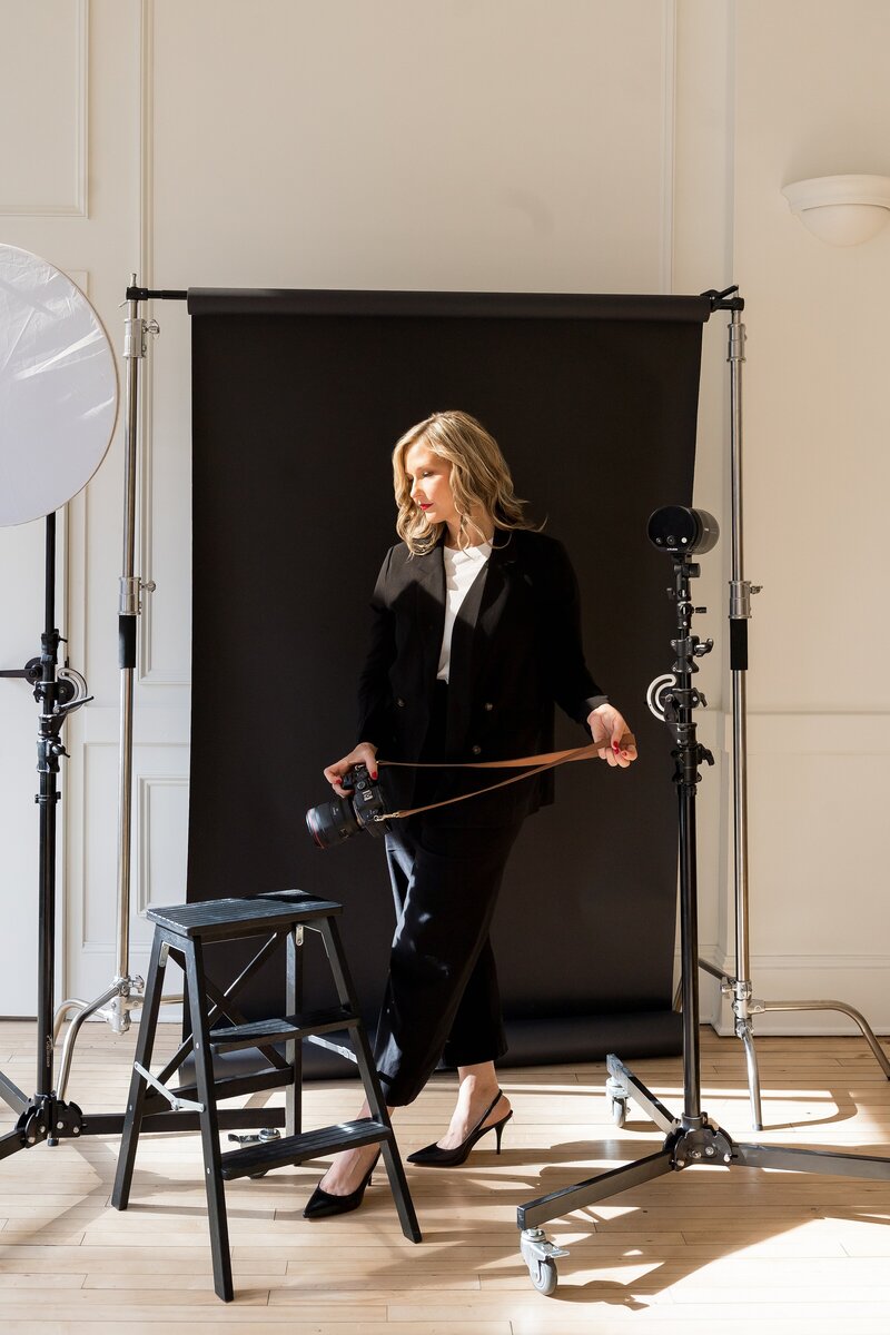 a photographer holds a camera in front of a black paper backdrop