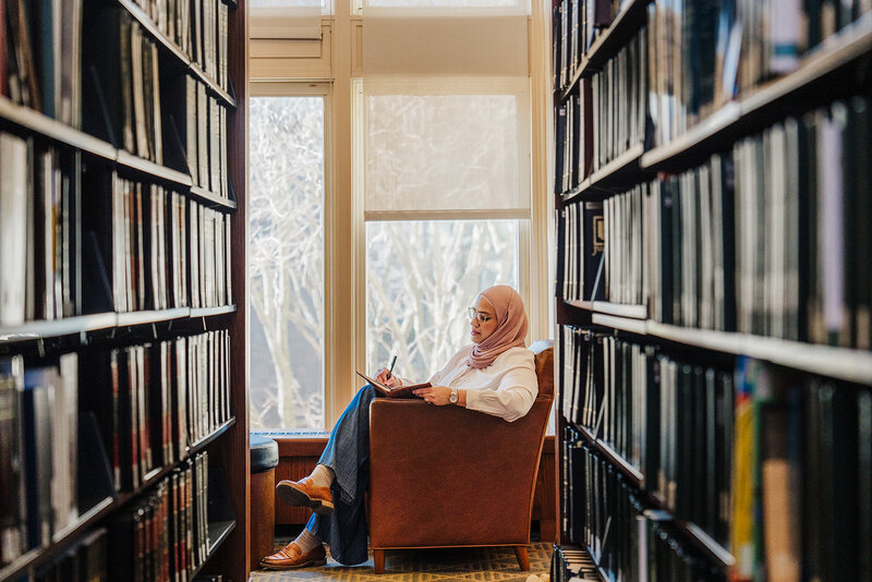 woman writes in notebook between library stacks at harvard in boston
