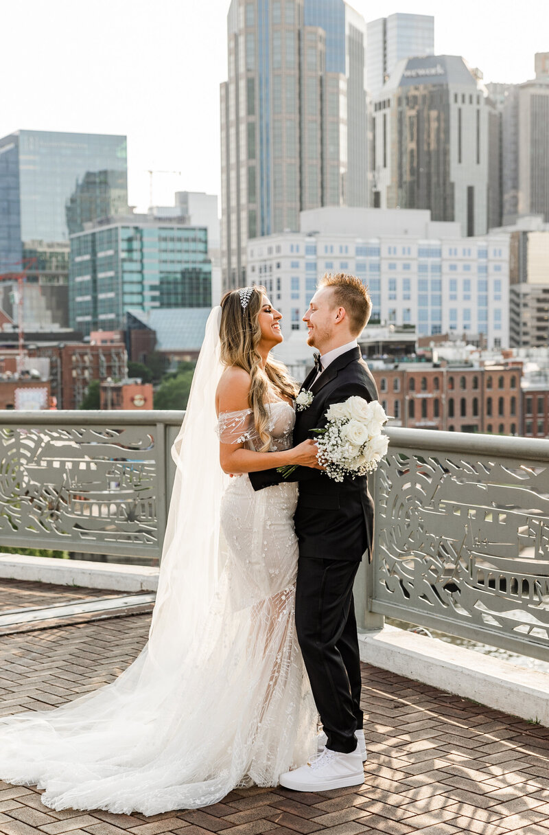 Bride and groom joyfully embracing on a balcony in front of tall skyscrapers
