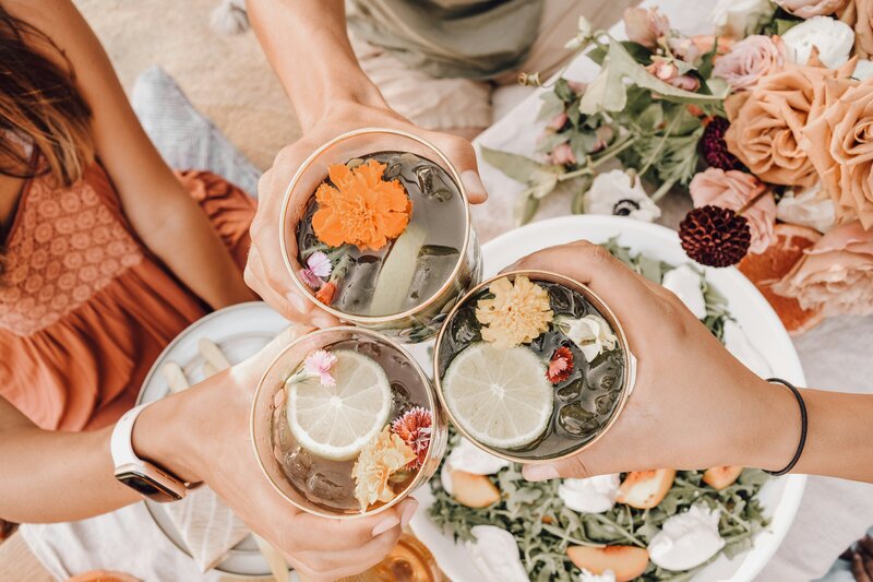 Friends toasting with floral drinks, celebrating holistic wellness.