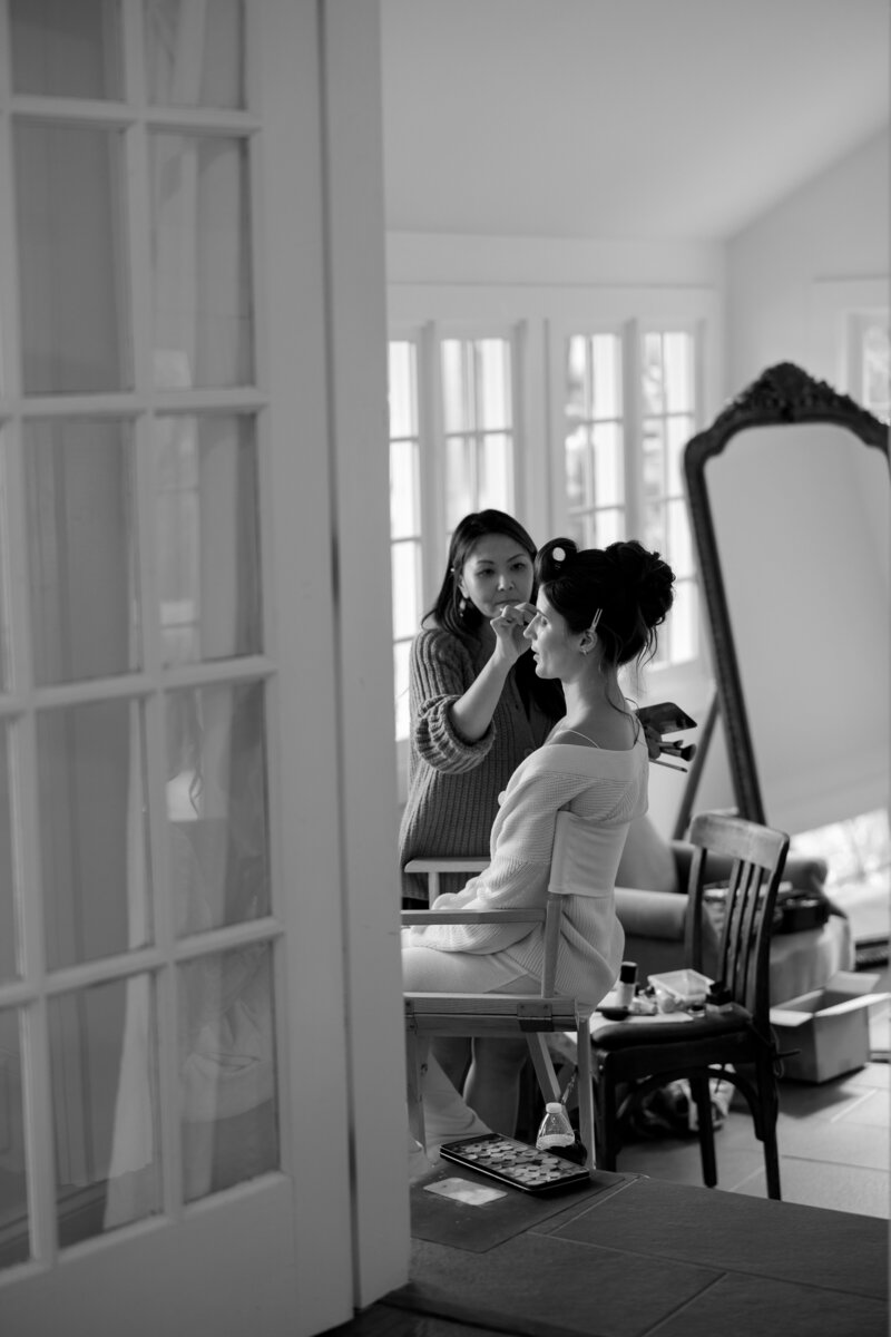 black and white shot of bride getting ready with makeup artist