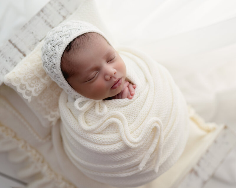 Profile view of a swaddled newborn in a white bonnet, styled with natural textures in a Paris, Ontario studio.