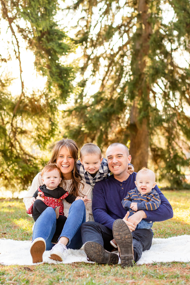 Mom dad twin babies and toddler smiling laughing sitting on blanket with pine tree backdrop