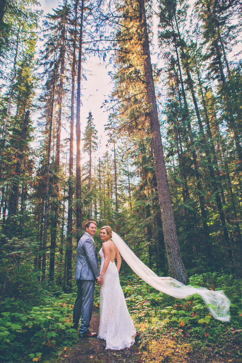 bride and groom waling in forest with veil blowing