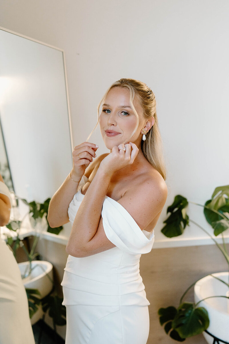 Bride getting ready in Columbus, OH, delicately putting on her earrings, a moment of anticipation before her wedding day.