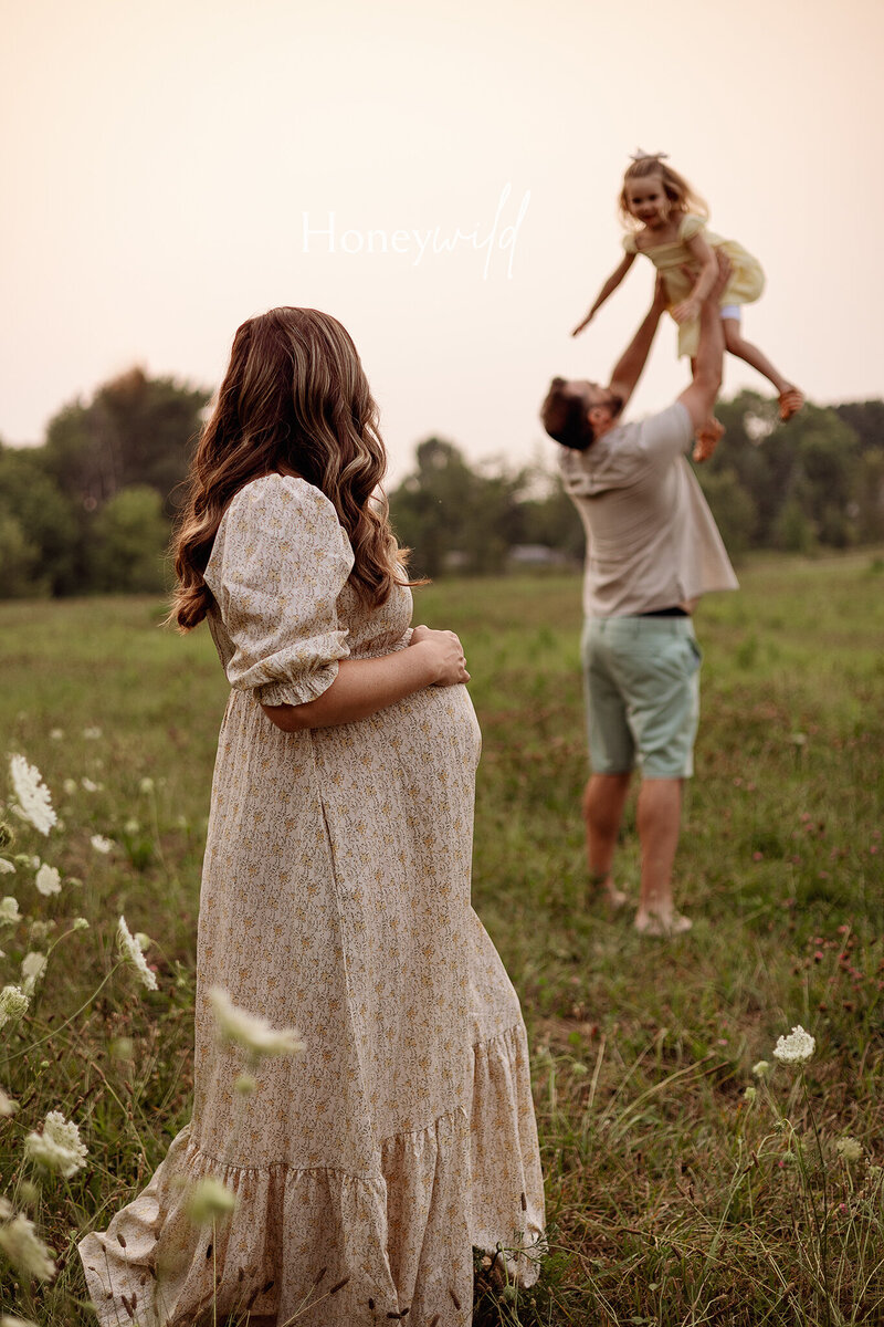 Maternity photography in Grand Rapids – pregnant mother holding daughter in wildflower field with partner