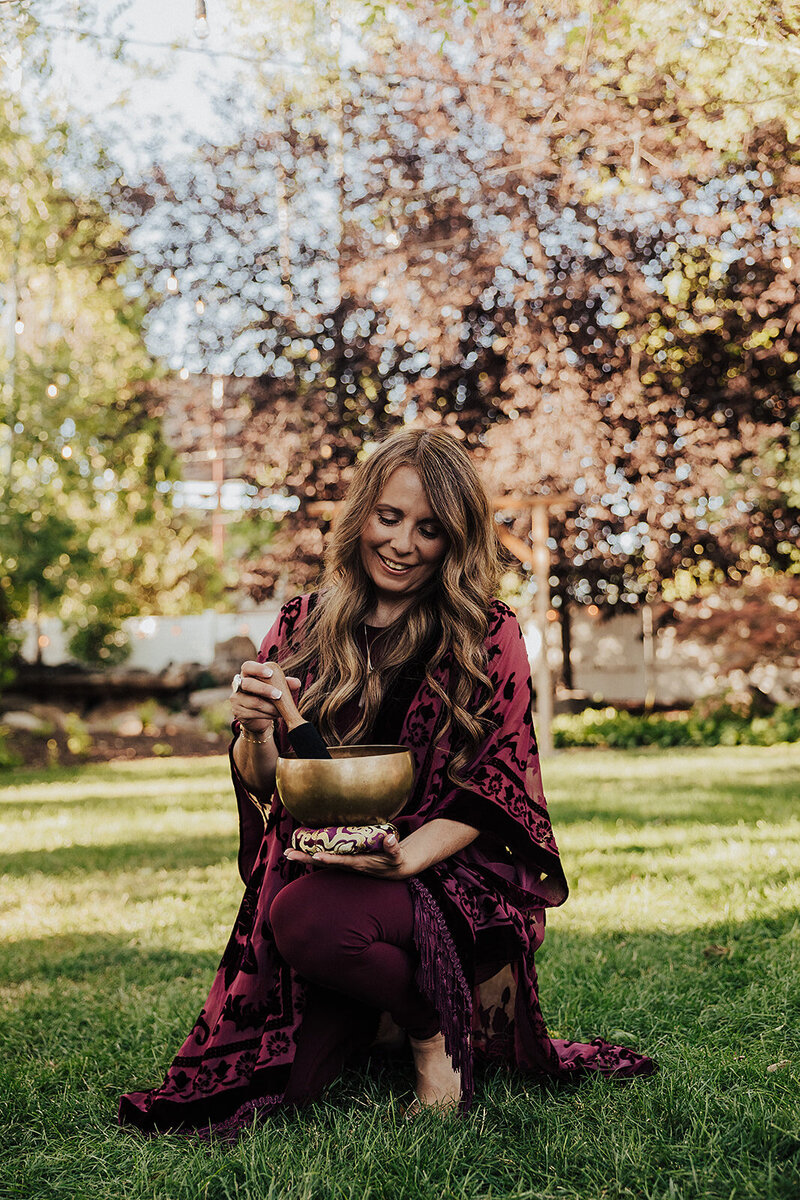 Patty in a maroon dress with her gold sound bowl outside 