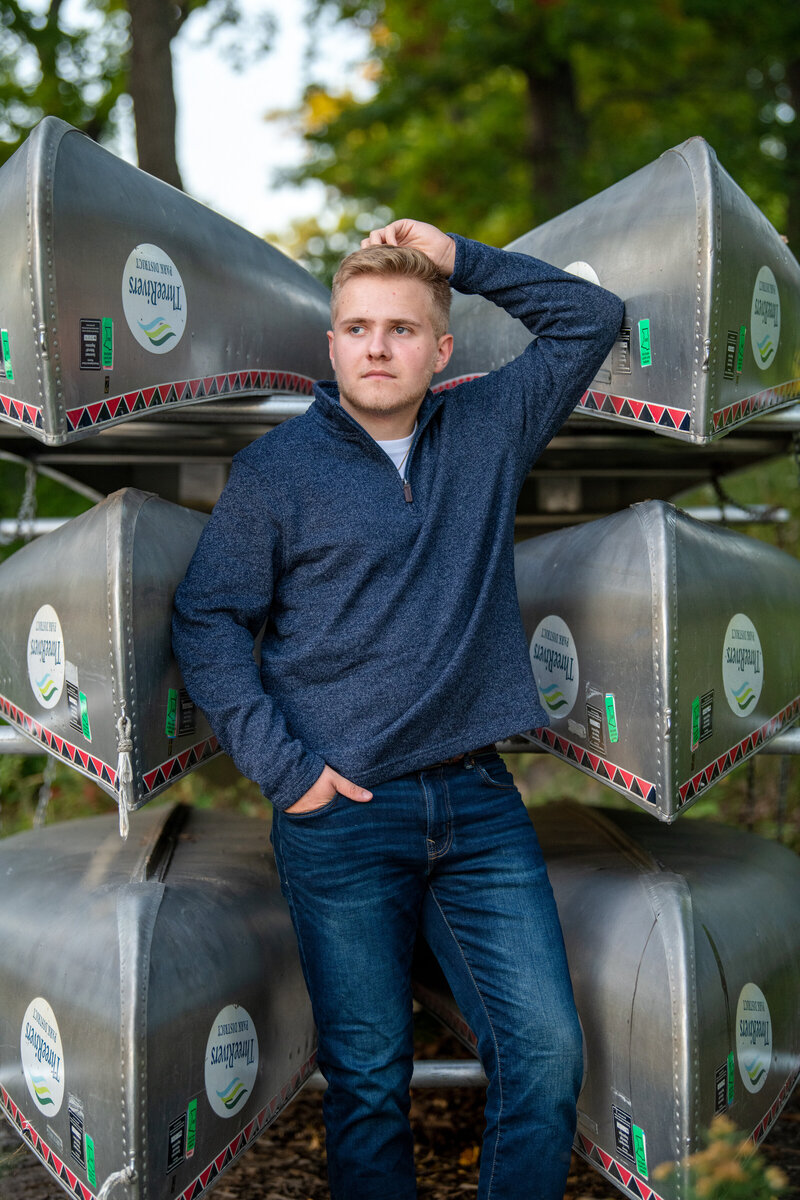 senior photo of guy in jeans and sweater with canoes