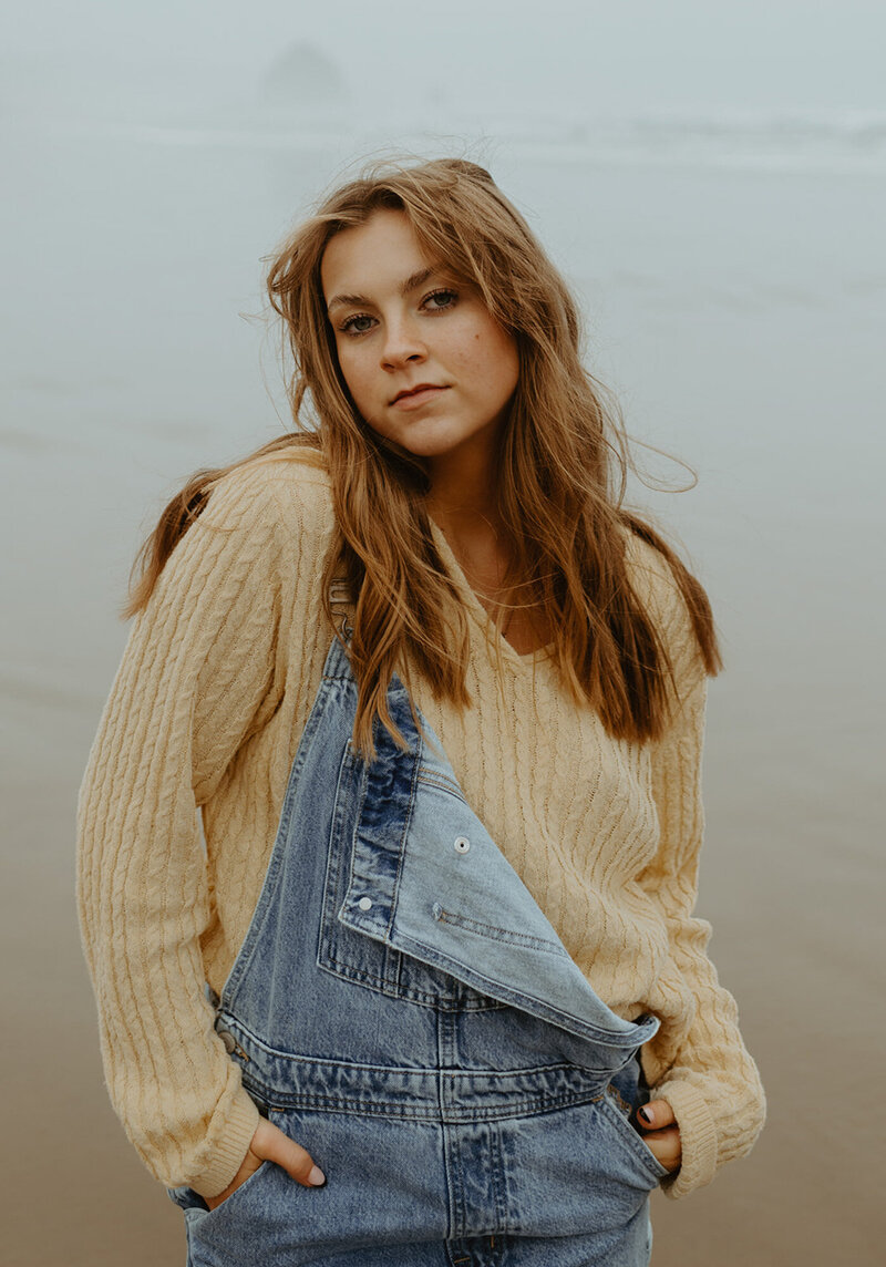 girl in sweater and overalls standing on oregon coast
