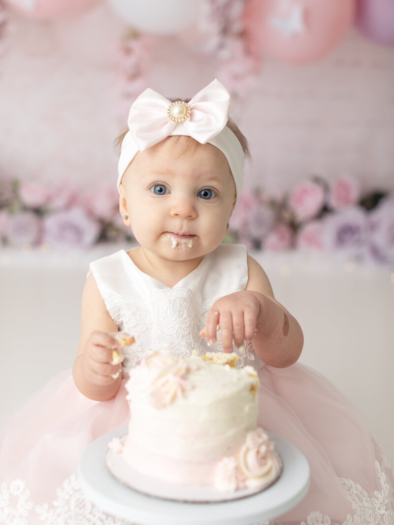 one year old girl in pink and white dress eating cake for cake smash