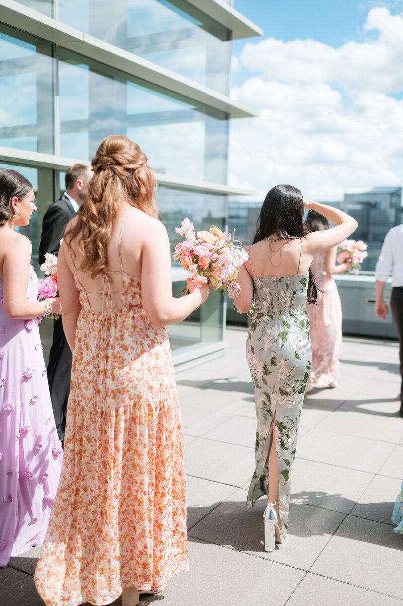 Groom in black tux and bride in asymmetrical wedding dress with a v neck smile at each other in front of The Farnam Hotel in Omaha, Nebraska. Photo by Anna Brace, an Omaha Wedding Photographers.