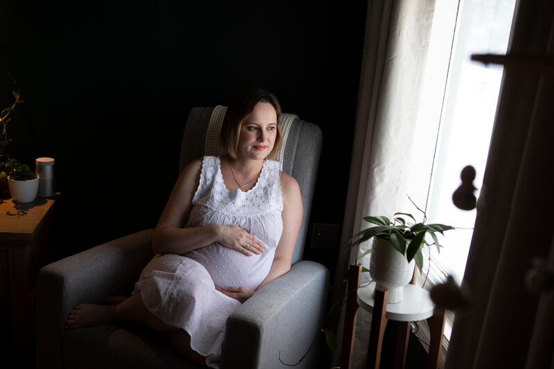 expectant mom holds her tummy and looks out window