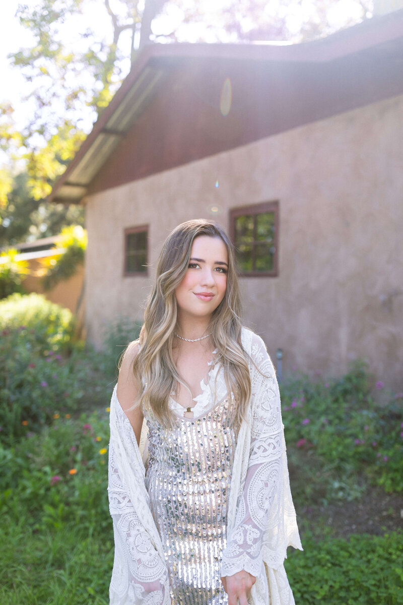 dirty blonde girl wearing silve sequin dress posing in front of a home