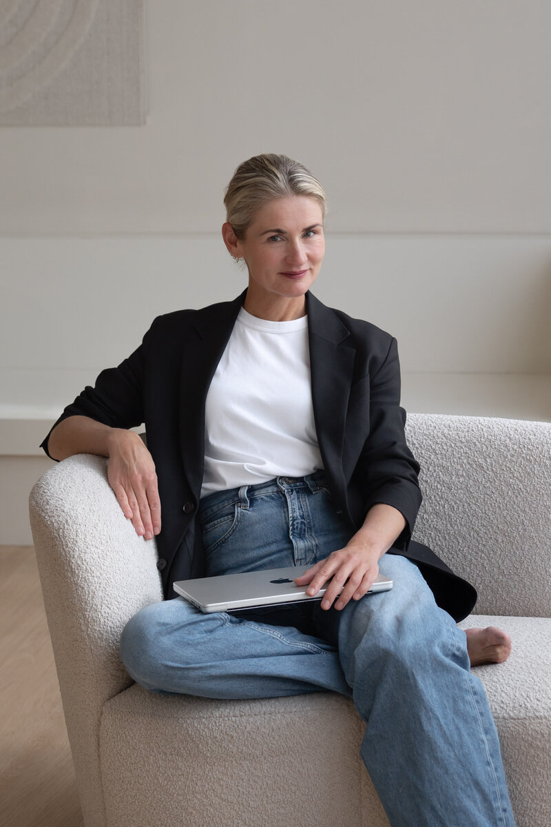 Coach en yoga docente Katinka de Bruin zittend op een stijlvolle stoel in een lichte studio.