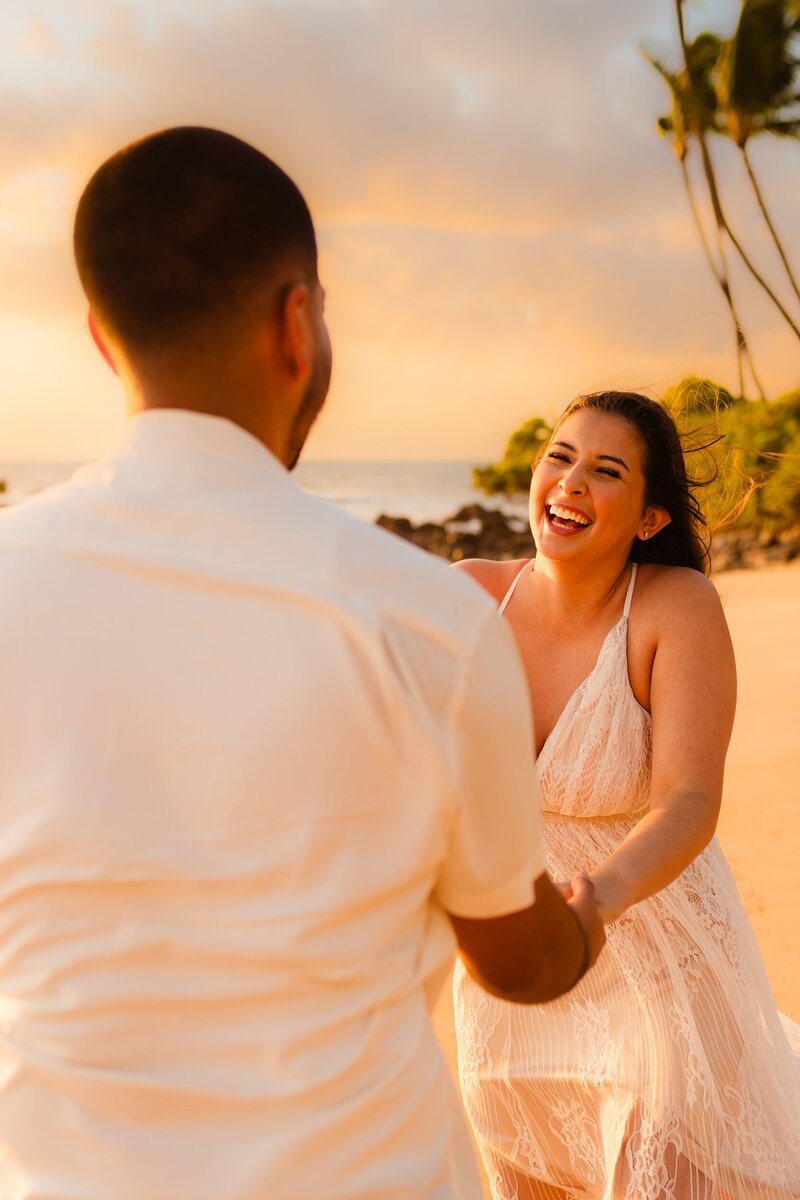 woman smiles and laughs at her fiance after he proposes with love and water on maui