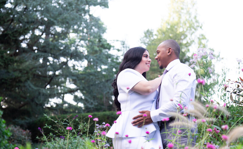 The couple is taking engagement pictures in a garden with colorful flowers. It is a bright and sunny day.
