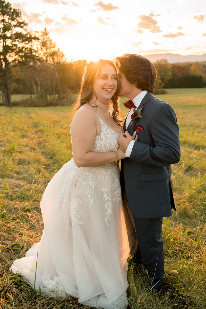 A groom is whispering a joke to his wife during their wedding photos at the barn in the mountains of Virginia.