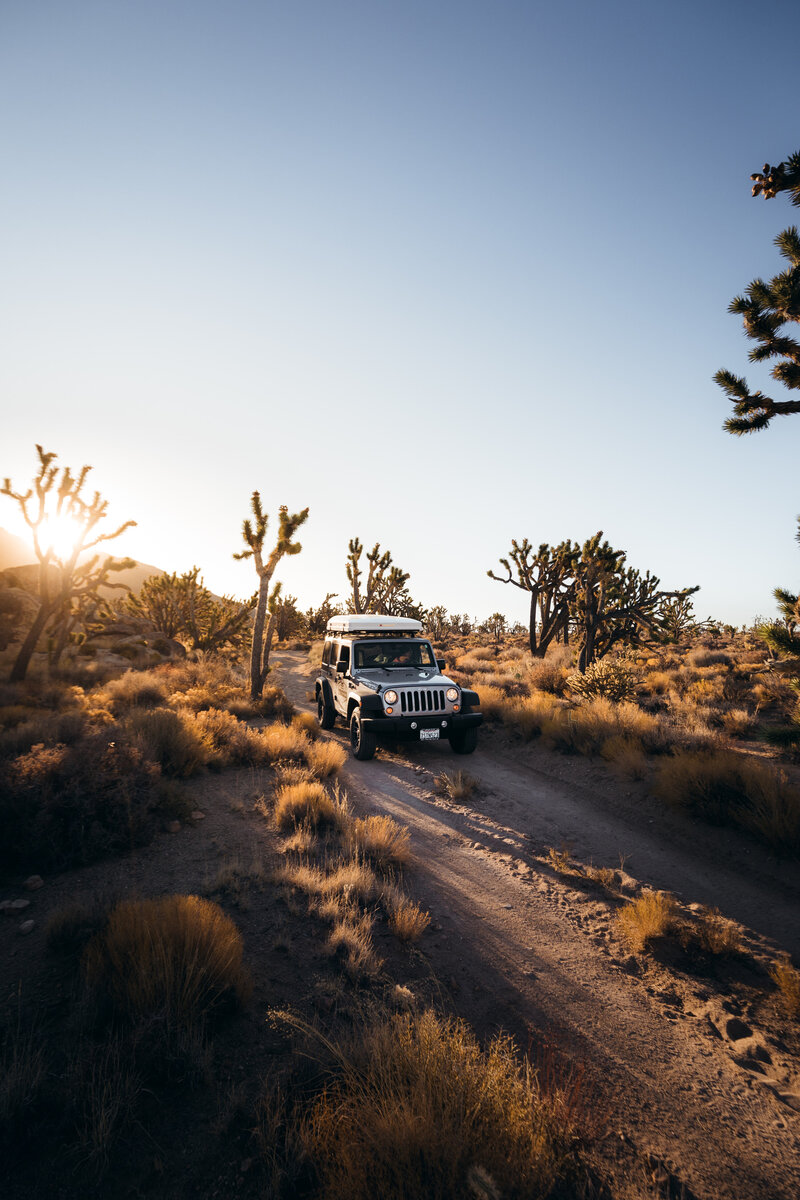Fully equipped Jeep driving through a scenic off-road trail in Joshua Tree at sunset, part of a curated luxury overland adventure with hidden camping locations