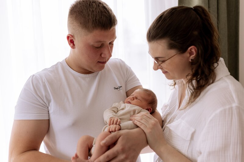 Vater steht neben Mutter und haelt Baby auf dem Arm