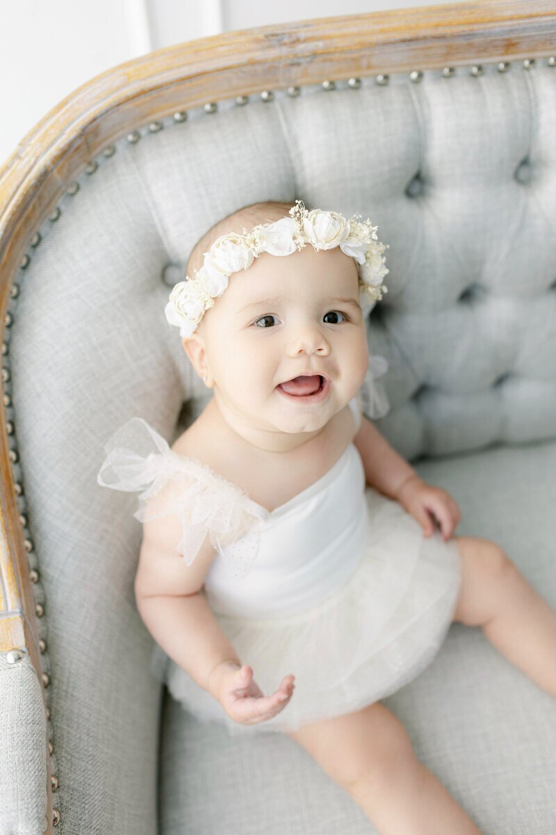Little baby sitting on bench and smiling by baby photographer nj