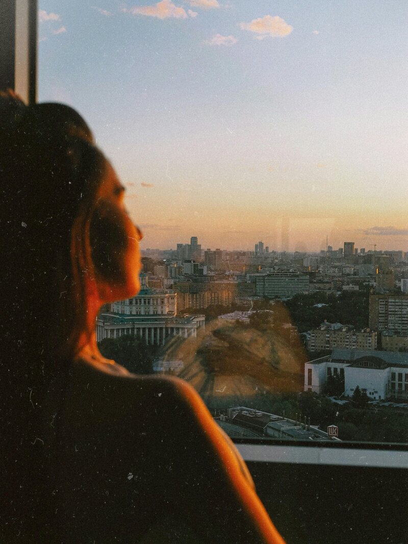 A film-style image of a woman looking out a window, representing OCD therapy for purely obsessional OCD and how it looks in her daily life.