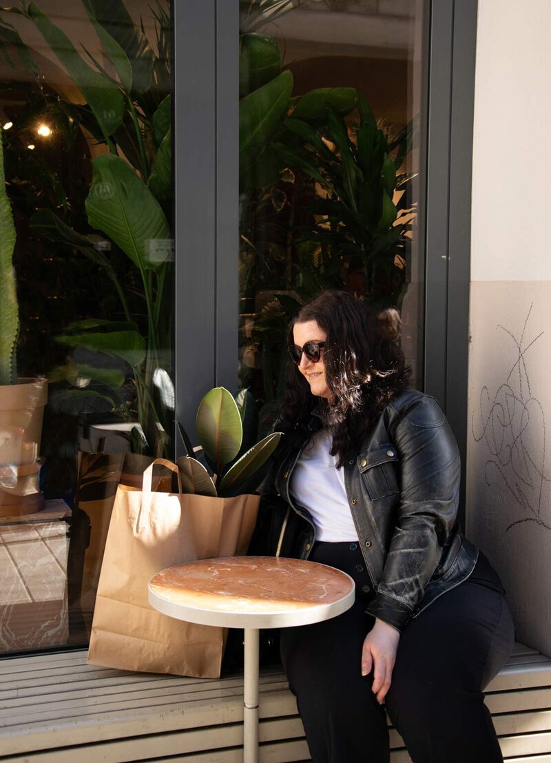 Martina Menzini sitting at outdoor cafe table surrounded by lush greenery.