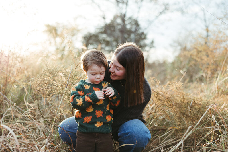 Mommy and me session of mother and son standing in a field looking at a leaf. 