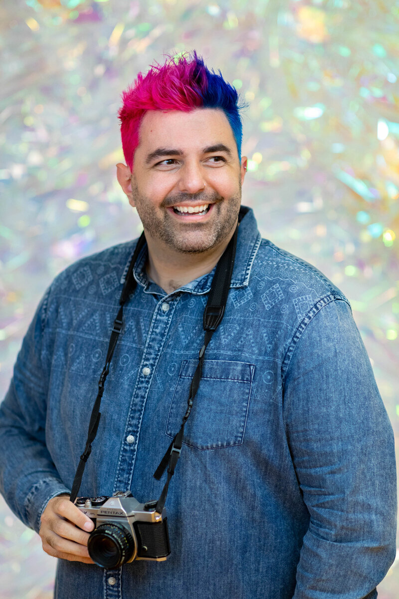 A photographer with bright colored hair and a camera around their neck.