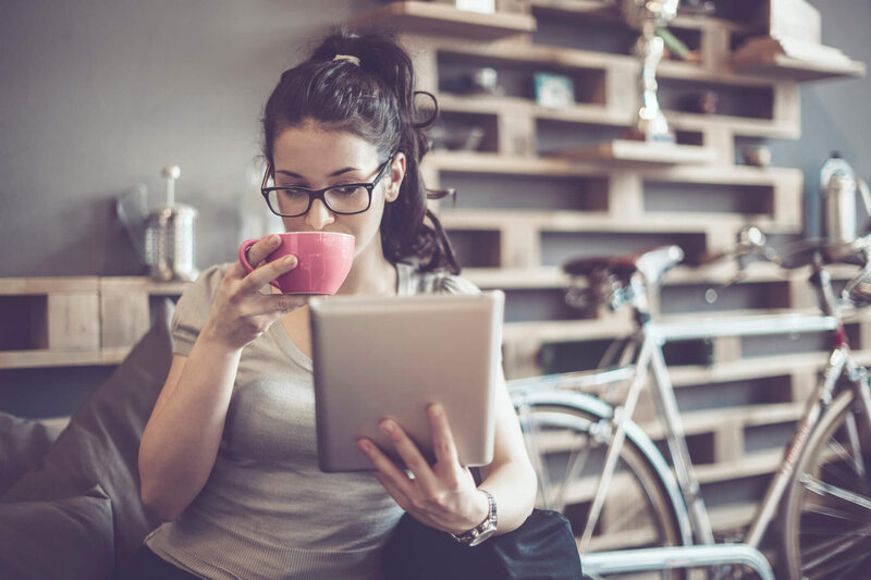 Young woman drinking tea from pink cup reading ipad