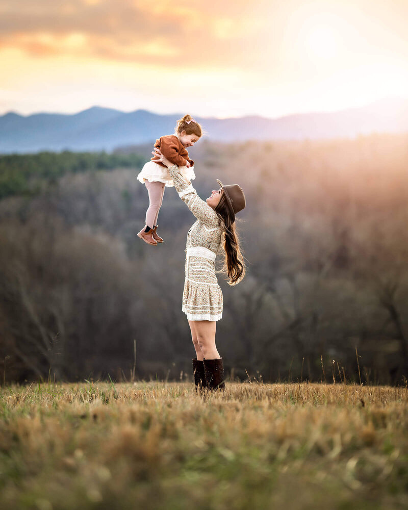 A mom and daughter playing airplane on a grassy hill at sunset on the Biltmore Estate in Ashevill