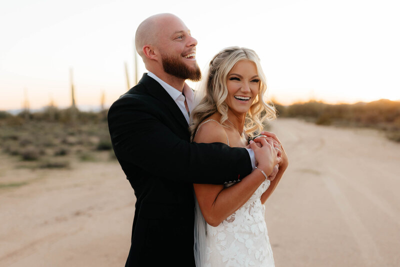 Groom holds bride from behind as they laugh on their wedding day