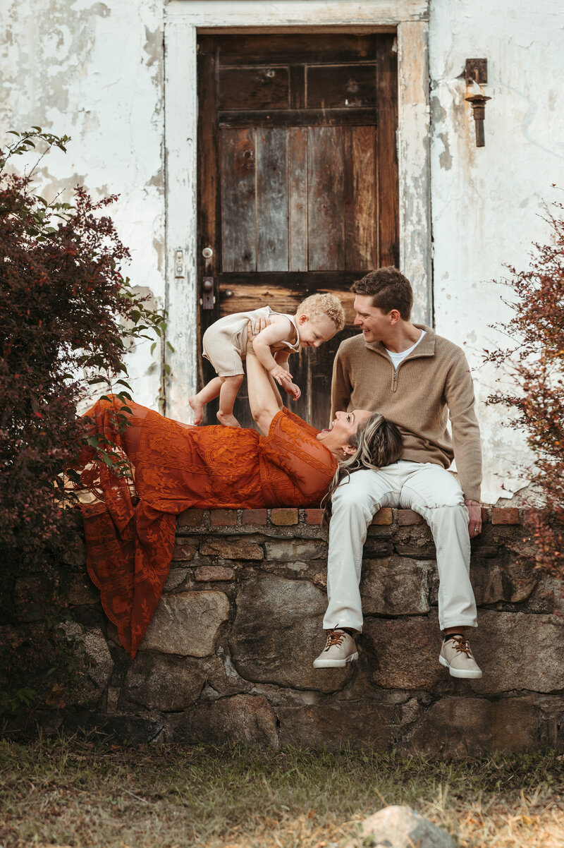 Family of three snuggling on a patio in coordinating clothing. 