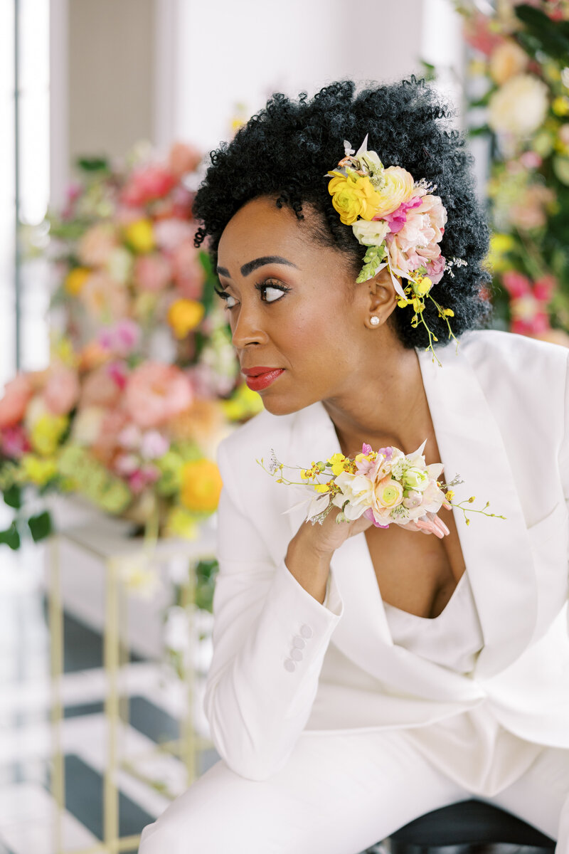 Bride in white suite with colorful flowers in hair.