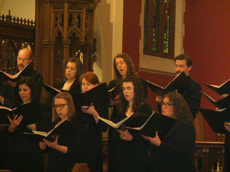 Stephanie holds a binder of music and sings in the front row of a choir concert in a church.