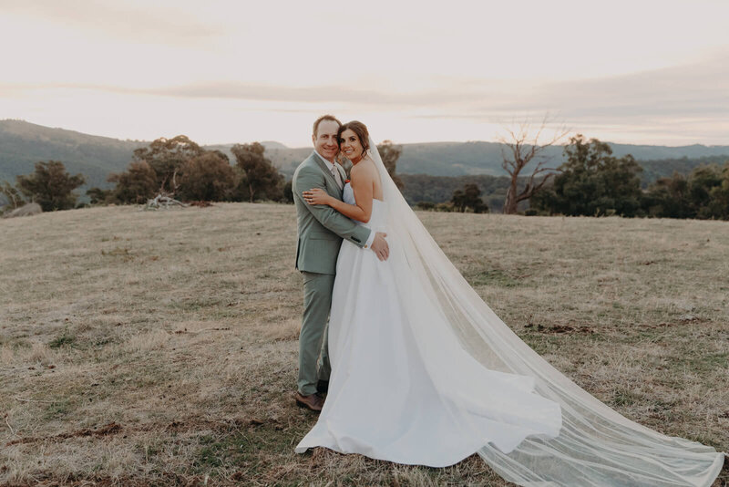 Bride and groom standing on hill at sunset