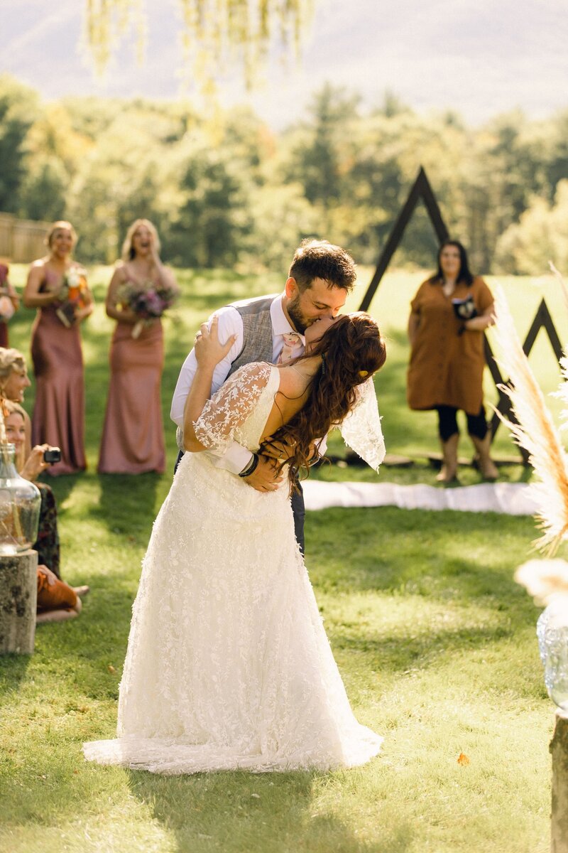 A groom leans the bride back for another kiss at the end of the wedding aisle.