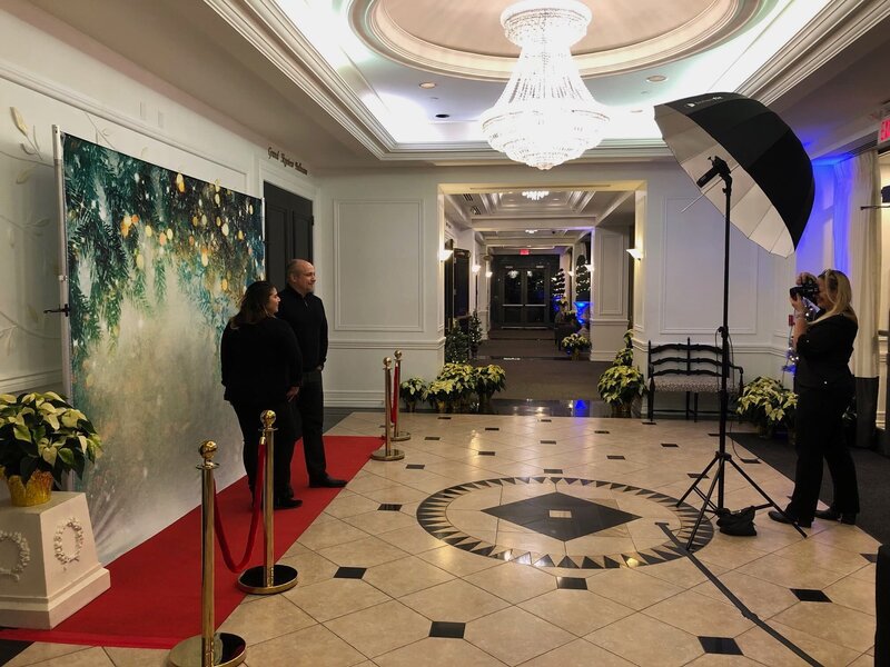 A professional event photographer capturing guests on a red carpet with festive decorations, supported by an onsite printing setup for immediate photo delivery