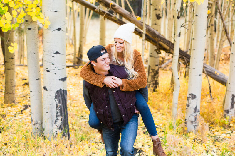 man giving fiance piggy back ride in Flagstaff fall leaves