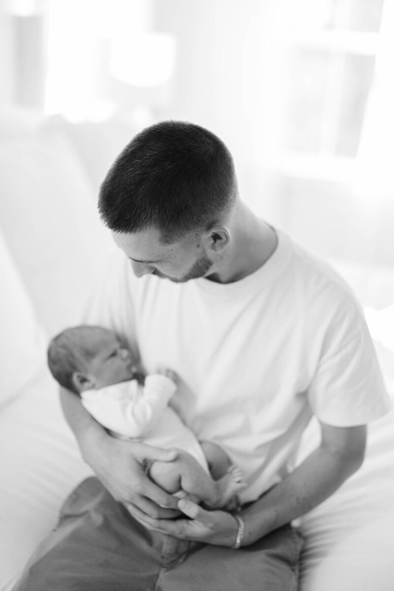 Father and newborn son sit together in black and white photo in nursery in Mechanicsburg, PA