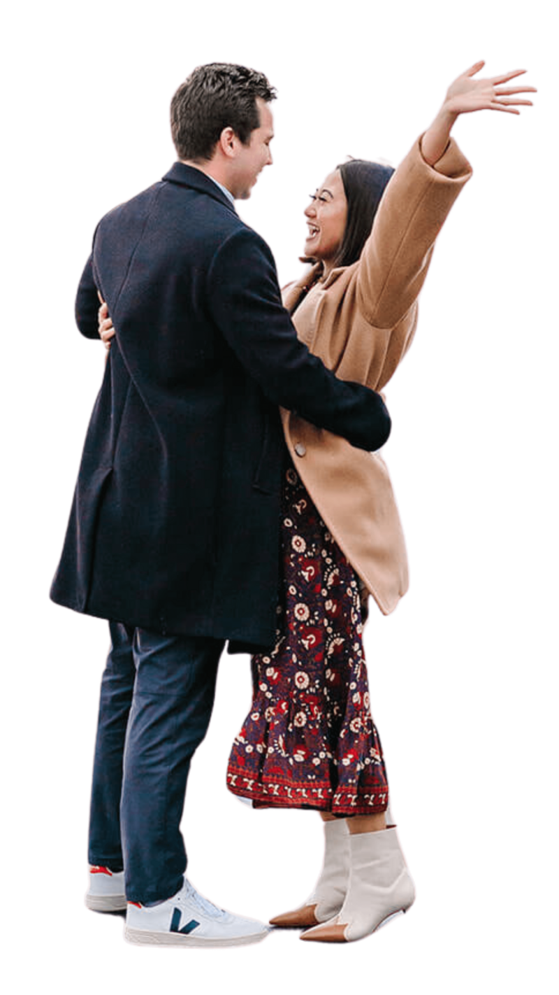 Man and woman hugging in celebration after a proposal near Sacré-Cœur in Montmartre, with the woman raising her hands in the air during a romantic Paris photoshoot.