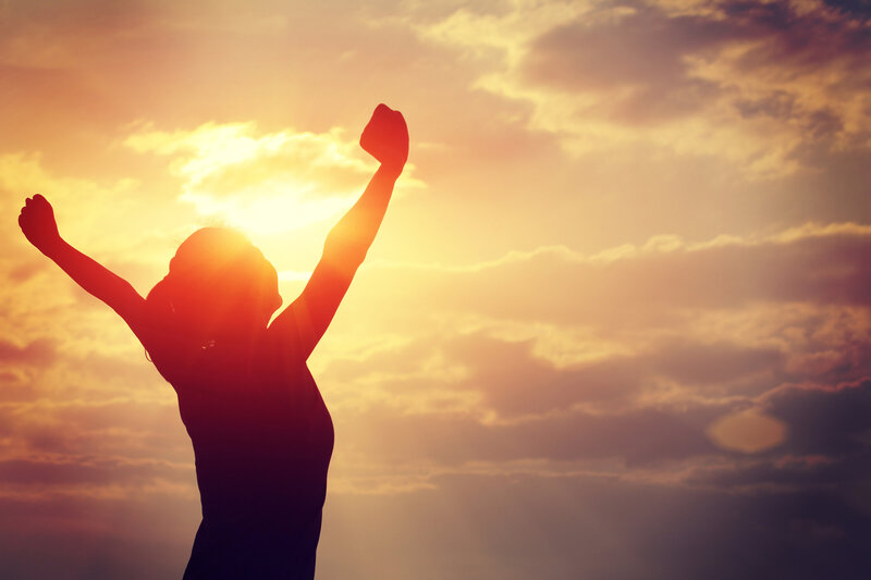 Woman holding her arms up in victory backlit by the sun