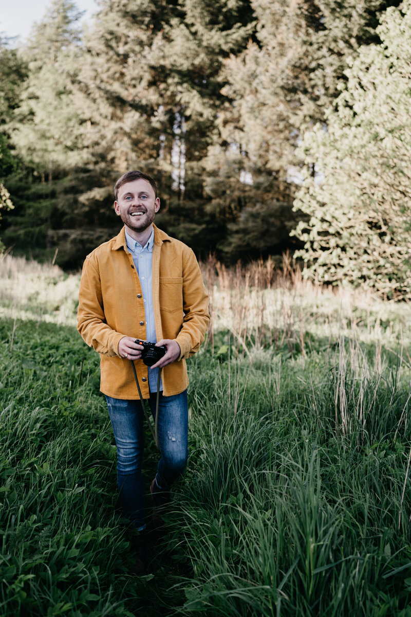 Aberdeenshire wedding photographer Scott Arlow walks through the woods holding a camera.