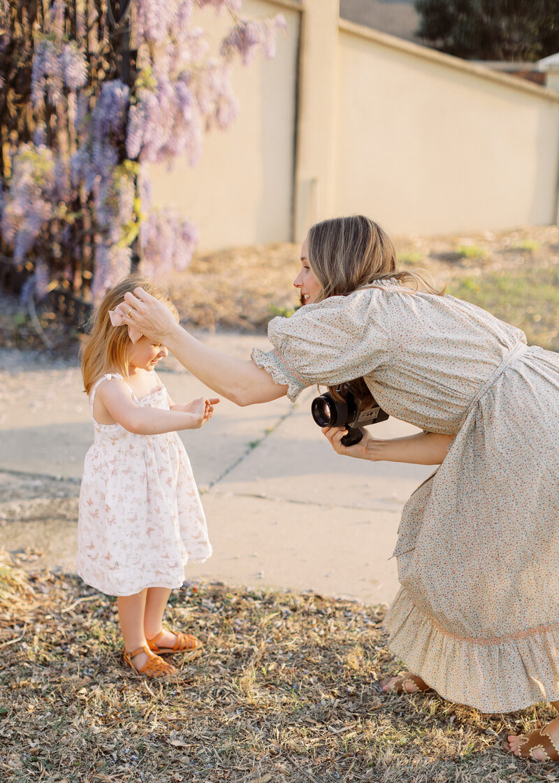 photographer holding camera adjusts hair of child preparing for photo to be taken in front of wisteria blooms