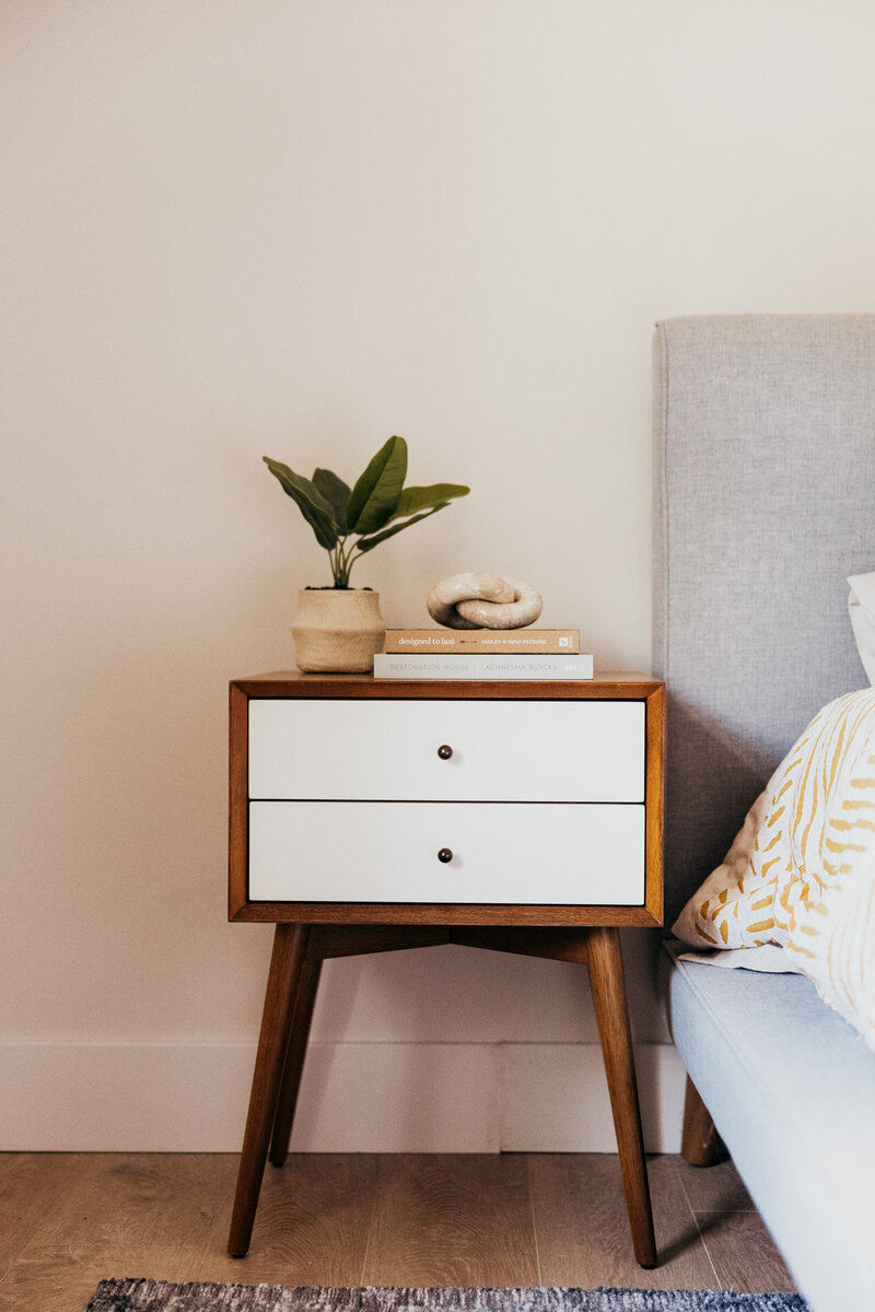 A close up of a wooden side table with white drawers, with books and a house plant on top of it. 