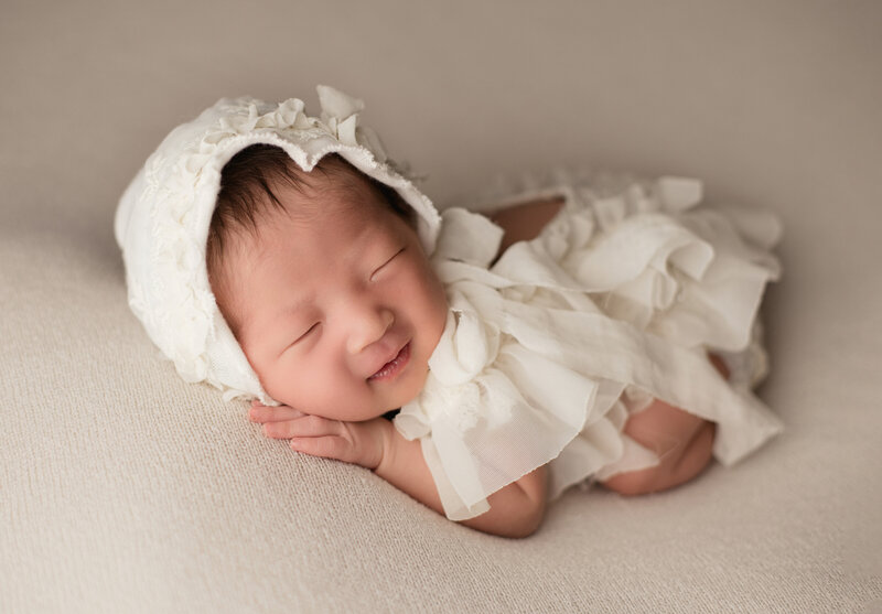 Photograph of Newborn baby girl smiling in studio. Captured by newborn photographer in studio