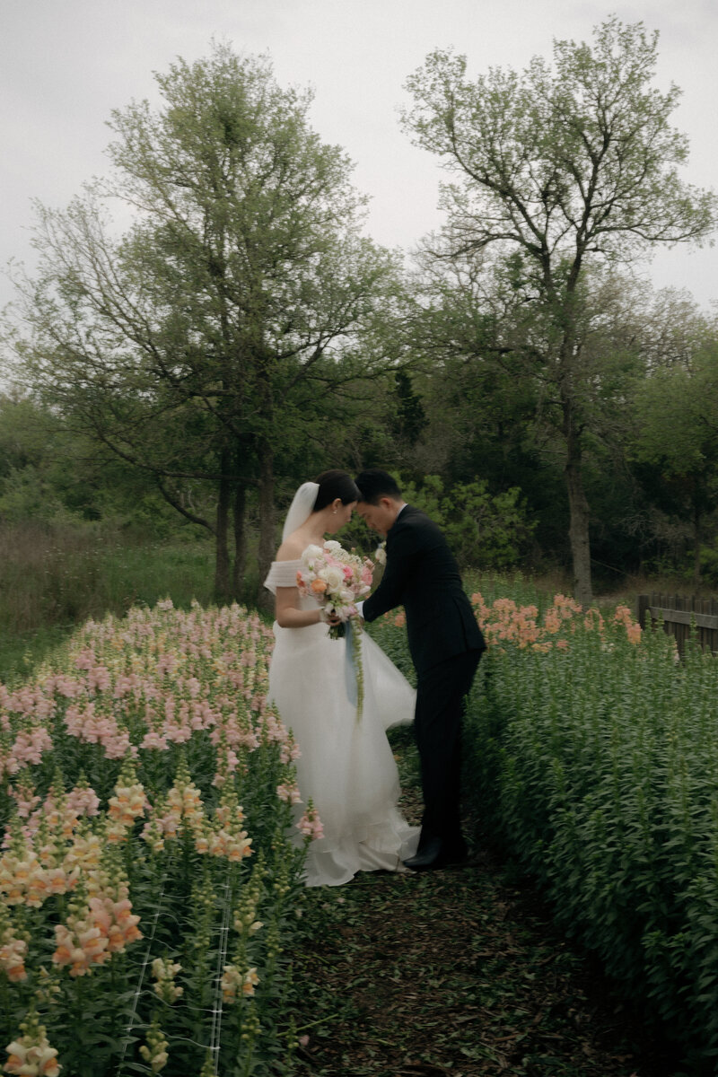 Groom holding train of bride's dress while they stand in a path of flowers